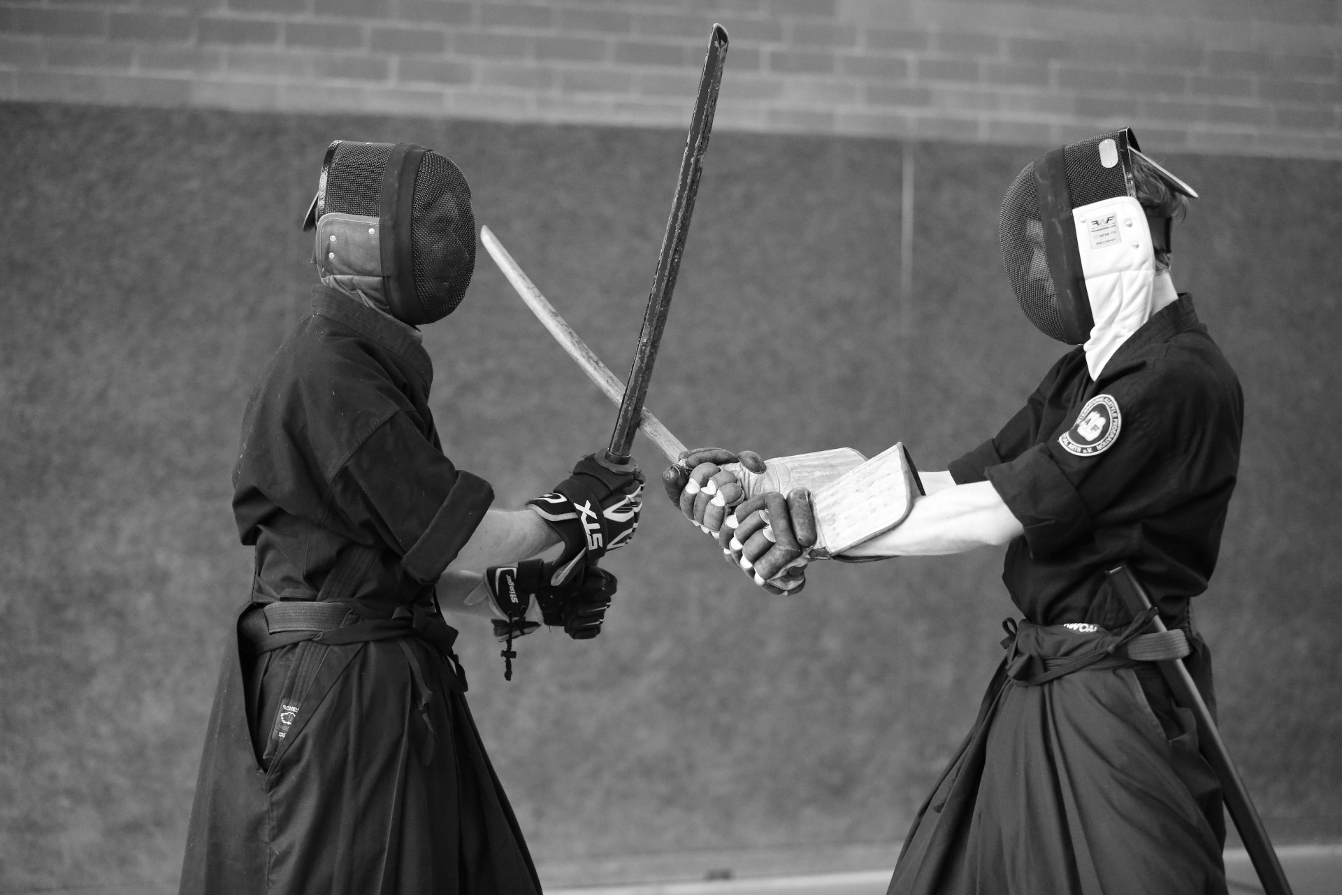 Zwei Personen mit Fechtmaske & Handschuhen kreuzen ihre Holzschwerter und stehen im Tsuba-Seriai
